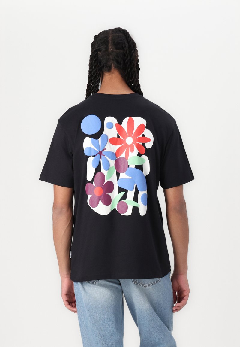 Sort t-shirt med et flerfarvet blomstermotiv på ryggen, med former i rød, blå og grøn mod en ensfarvet baggrund.