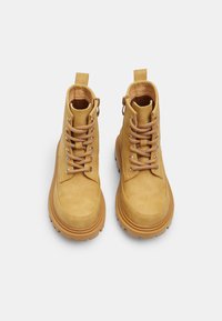 Bottines en cuir jaune, au toucher lisse, avec des bouts ronds, des œillets en métal et des lacets beiges. Comprend des languettes pour un enfilage facile.