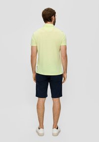 Jasnożółta krótko rękawowa koszulka polo o teksturowanym wykończeniu, w połączeniu z granatowymi szortami. Model ma na sobie białe sneakersy.