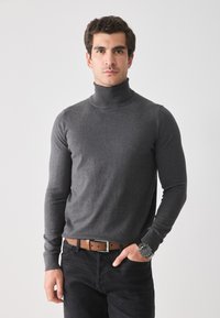 Suéter gris de cuello alto con mangas largas, hecho de una tela suave; combinado con jeans oscuros y un cinturón de cuero marrón, con hebilla plateada.