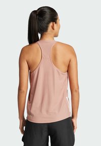 Roze sportieve tanktop met een racerback ontwerp, gemaakt van lichtgewicht, ademend materiaal. Voorzien van een logodetail aan de zijkant. Zwarte shorts zichtbaar.