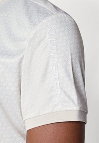 Chemise de golf à manches courtes en beige clair avec un motif géométrique. Dotée d'un col côtelé et d'un logo brodé sur la manche.