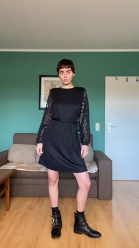 Črna obleka z čipkastimi rokavi, pritisnjena v pasu s trakcem enakih barv. Ima okrogel izrez, mehko teksturo in sproščen kroj. Črni gležnjarji.