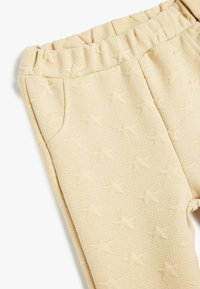 Beige Hose mit Sternmuster und elastischem Bund, strukturierter Stoff und Seitentasche. Weiches, gemütliches Material, ideal für Freizeitbekleidung.