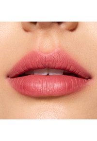 Rouge à lèvres mat sur les lèvres, avec une teinte rose pâle. Les lèvres ont une texture lisse avec de légères stries. Fond de teint naturel.