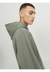 Hanorac oversized verde deschis, cu glugă prevăzută cu șnur, având o textură moale și o croială confortabilă. Detalii de cusătură vizibile pe margini.