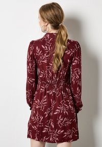Abito bordeaux con maniche lunghe, vita elastica e motivo a foglie in rosa chiaro. Tessuto morbido con una vestibilità rilassata, design a lunghezza ginocchio.