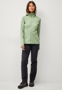 Lys grøn zip-up jakke med en tætsiddende design, parret med sorte cargo bukser med lommer, afsluttet med sorte vandrestøvler.