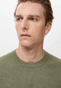 Green knit sweater with a round neckline, featuring a textured pattern. Model has facial features partially visible, with light skin tones.