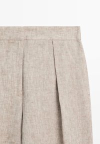 Beige linnen stof met verticale plooien en een tailleband, met details van textuur en stikwerk.