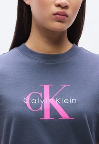 Γκρι βαμβακερό T-shirt με μεγάλο ροζ και λευκό λογότυπο «Calvin Klein», με στρογγυλή λαιμόκοψη και κοντά μανίκια.