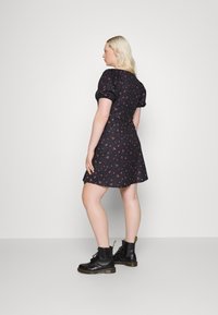 Vestido preto com padrões florais, mangas bufantes e saia evasê. Usado com botas de tornozelo pretas com atacadores. O vestido apresenta pequenos padrões de flores vermelhas e rosas.