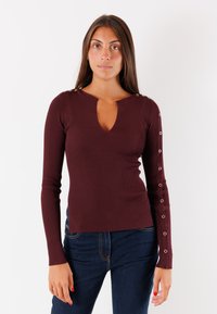 Top a maniche lunghe bordeaux a coste con scollatura a chiave e borchie decorative sulle spalle e sulle maniche. Texture morbida, design aderente.