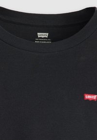 Crna pamučna majica s rebrastim okruglim izrezom i malim crvenim Levi's logotipom na lijevoj strani prsiju. Jednostavan dizajn, bez uzoraka.
