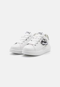 Adidași albi cu superior din piele texturată, vârf rotund și închidere cu șireturi. Prezintă un accent contrastant negru și un charm decorativ atașat.