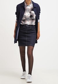 Gonna a tubino in denim di colore blu scuro con dettagli di cucitura, abbinata a una camicia a quadri con bottoni e uno strato esterno blu navy. Sneakers bianche completano il look.
