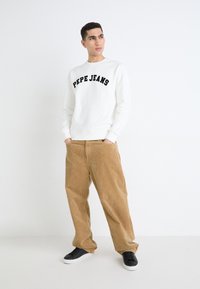 Fehér pulóver "PEPE JEANS" felirattal fekete betűkkel, bézs kordbársony nadrággal és fekete tornacipővel párosítva. Egyszerű, laza fazon.