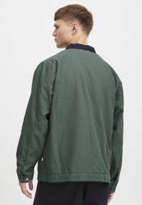 Grønt bomuldsjakke med krave, lange ærmer og knaplukning i ærmerne. Glat tekstur, enkelt design og afslappet pasform. Vist bagfra.