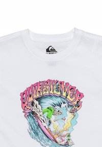 Camiseta de algodón blanca con un diseño gráfico colorido de un esqueleto surfeando una ola, con el texto "Quiksilver" en una fuente negrita y estilizada.