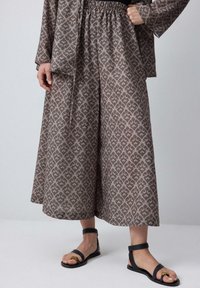 Šedý vzorovaný outfit s voľným topom a širokými nohavicami. Materiál má textúrovaný povrch. Čierne sandále na opätku dokončujú vzhľad.