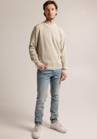 Light beige ribbed sweater with high collar, paired with light blue jeans and white sneakers. The fit is casual, with a relaxed silhouette.