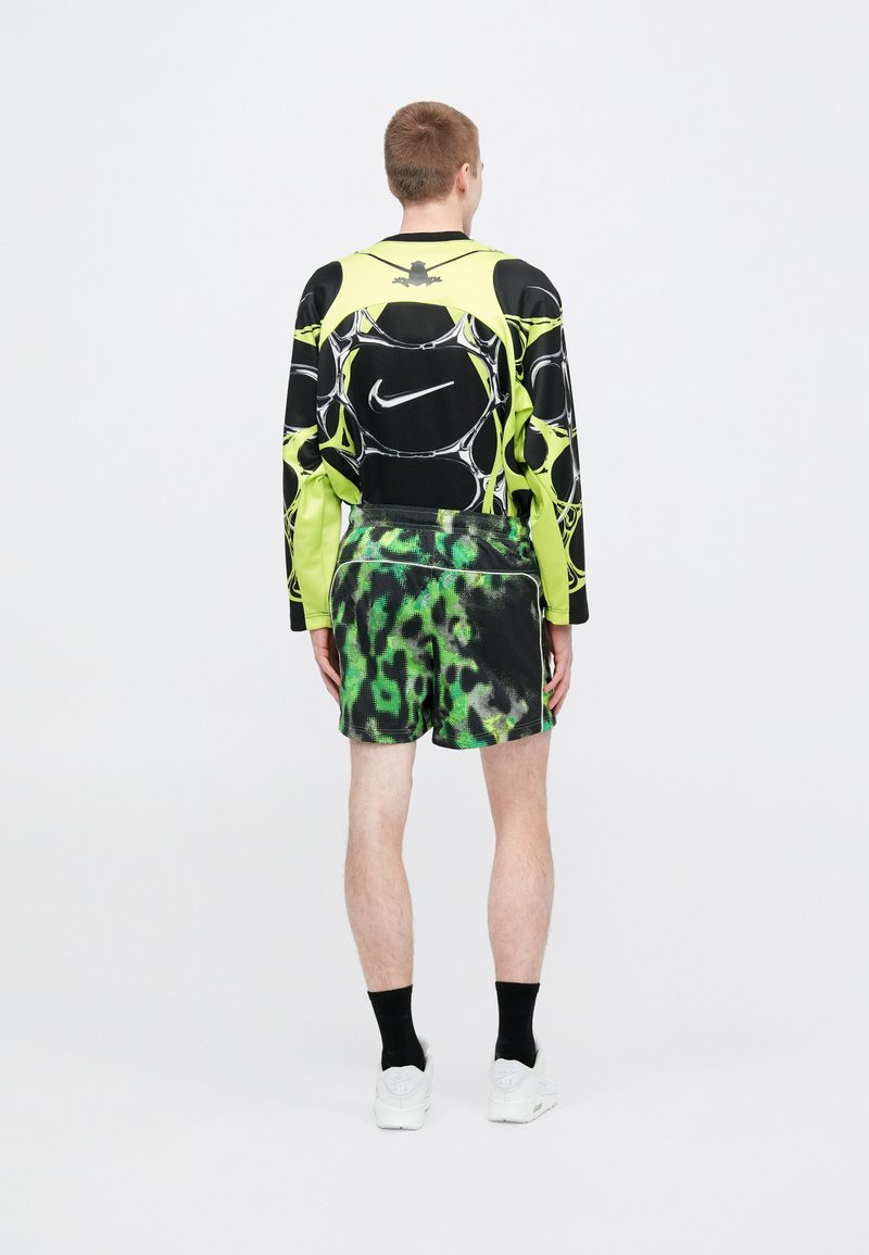 Black and neon green long-sleeve top with abstract pattern and logo; matching black shorts with green tie-dye pattern; white sneakers.
