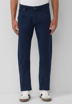 Marineblaue Baumwollhosen mit geradem Bein, ausgestattet mit einem Standardbund, Fronttaschen und dezenten Steppdetails, kombiniert mit weißen Sneakers.