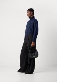 Navy quarter-zip sweatshirt with ribbed cuffs, paired with black wide-leg trousers. Holding a small black leather handbag with a strap.