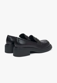 Zwarte leren loafers met een ronde neus, dikke zolen en schuine uitsparingen aan de voorkant. Glad textuur met subtiele stiksels.