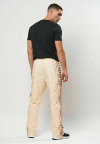 Világos krémszínű melegítőnadrág fekete logómintával az oldalfelületeken, egyszínű fekete pólóval párosítva. Sima textúra és laza szabás.