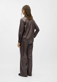 Ensemble en simili cuir marron comprenant une chemise et un pantalon large. La chemise présente un ourlet arrondi et des poignets boutonnés. Texture lisse avec un léger éclat.