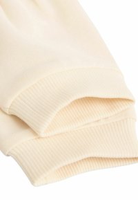 Material din bumbac de culoare bej deschis, cu textură ribbed, având două margini îndoite. Materialul pare moale și flexibil, potrivit pentru îmbrăcăminte casuală.