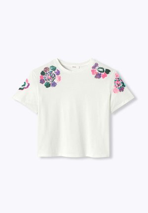 Chemise blanche à manches courtes avec col rond, présentant des motifs floraux colorés en perles sur les épaules et les manches.