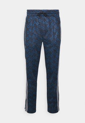 Marineblauwe trainingsbroek met een herhalend blauw "G"-patroon, elastische tailleband met trekkoord, zijzakken met rits en witte zijstrepen.