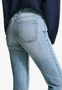 Svetloblue džins kroja, ki se prilega telesu, z visokim pasom in dvema zadnjima žepoma, ki ima subtilno zbledelo teksturo in klasično šivanje.