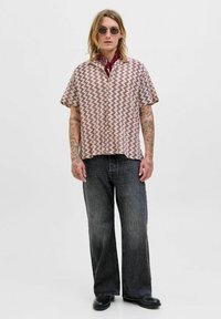 Camicetta a maniche corte con un motivo a zigzag in beige e bordeaux, abbinata a jeans a palazzo grigi scuri e stivali neri.