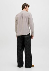 Lysebrun skjorte med lange ærmer og rygpåsætning, parret med brede sorte denimbukser. Stoffet ser blødt ud med en subtil tekstur.