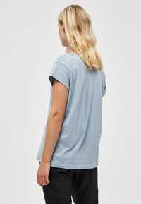 Světle modré bavlněné tričko s krátkými ohrnutými rukávy, volným střihem a jednoduchým designem. Tkanina má mírně strukturovaný povrch.