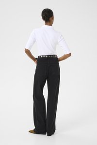  svarte høyt liv brede ben jeans med en midje fremhevet av sølvknapper; parret med en tettsittende hvit polo skjorte.