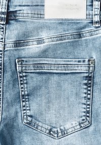 Jean en denim bleu clair avec une poche arrière distinctive, présentant des coutures dorées, une étiquette en cuir et une texture légèrement délavée.