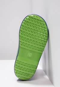 Semelle en caoutchouc verte d'une chaussure, présentant un motif en zigzag et une texture antidérapante, avec un accent bleu autour des bords et le numéro "21" en relief.