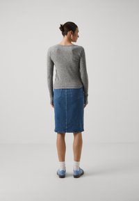 Grå ribbet genser med lange ermer, kombinert med et blått denimskjørt som har to baklommer og en rett silhuett.