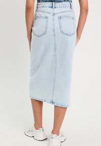 Gonna midi in denim blu con taglio dritto, caratterizzata da vita alta, tasche posteriori e orlo sfrangiato. Indossata con sneakers bianche.