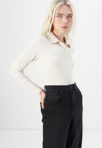 Cream ribbed long-sleeve polo top with a collar and button placket, paired with high-waisted black jeans featuring front pockets.