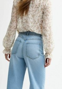 Jasna bluzka w kwiatowy wzór z bufiastymi rękawami, w zestawieniu z jasnoniebieskimi, wysokim talii jeansami w szerokim kroju, posiadającymi dwie tylne kieszenie.