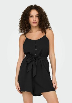 Une combinaison noire sans manches avec des boutons frontaux, des bretelles réglables et une ceinture à nouer à la taille. Matière douce et coupe décontractée.