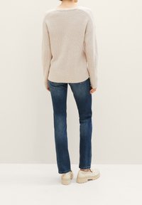 Beige stickad tröja med en lös passform, texturerat mönster och sänkta axlar, tillsammans med mörkblå jeans och ljusa plattformsskor.