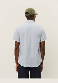 Kortermet skjorte i lyseblå med hvite vertikale striper. Har en avslappet passform og buet søm. Kombinert med en khaki caps.