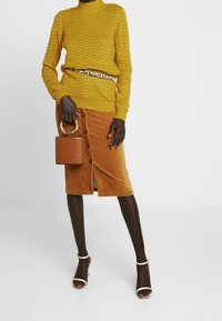 Żółty sweter dziergany z falistym wzorem, połączony z brąską spódnicą z korduroju z guzikami i rozporkiem. Uzupełniony niewielką torebką o fakturze krokodyla.