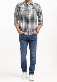 Czarna i biała koszula flanelowa w kratę, z długimi rękawami, dwoma kieszeniami na piersi, w zestawie z niebieskimi dżinsami i białymi trampkami.